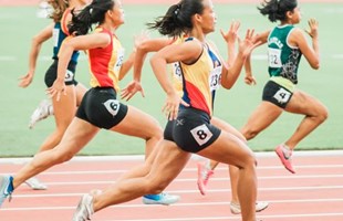 Five women running on an athletics track. The view is from the side as the runners go past.