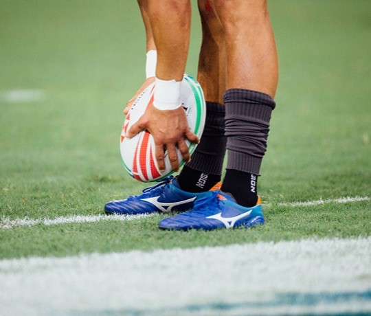 Male rugby player holding a rugby ball as he places it on the ground. 