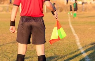 Image of the back of a linesman standing at sidelines of football pitch with players in the distance. 