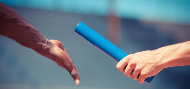 Close up image of a relay baton being passed from one persons hand to another. 