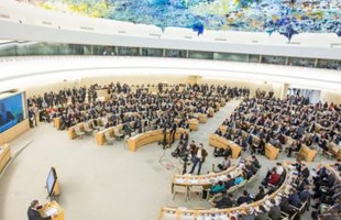 Bird's-eye view of people sat in the Human Rights Council room in Geneva, underneath the colourful textured 