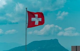 Swiss flag against bright blue cloudy sky. 