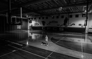 Black and white image of basketball player alone on a basketball court indoors.